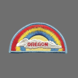 May include: Embroidered patch featuring a rainbow design with red, yellow, and blue colors. The word "OREGON" is embroidered in red across a white cloud. The patch has a blue border.