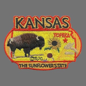 May include: An embroidered patch with a yellow background and red border. The patch features the words "Kansas" and "The Sunflower State" in red and black lettering. The patch also features a brown bison, a sunflower, and the word "Topeka" in red lettering.