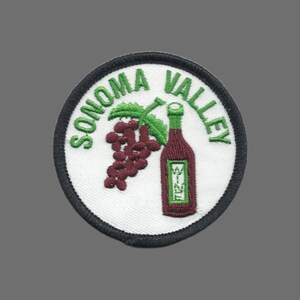 May include: Embroidered patch with a white background, black border, and the words "SONOMA VALLEY" in green. Features a cluster of purple grapes and a wine bottle with the word "WINE" on it.
