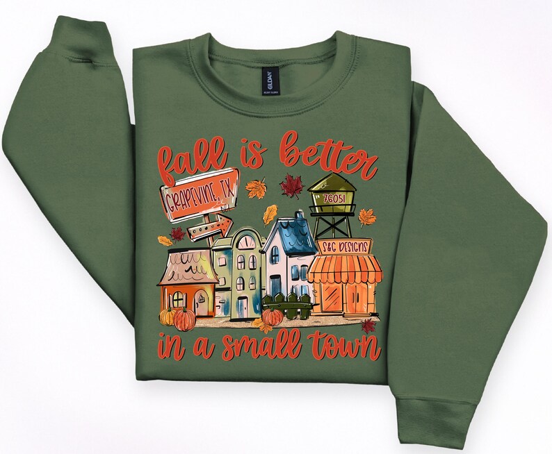 May include: Green sweatshirt with a colorful graphic that reads "Fall is better in a small town." The graphic features a town scene with houses, pumpkins, and the text "Grapevine, TX."