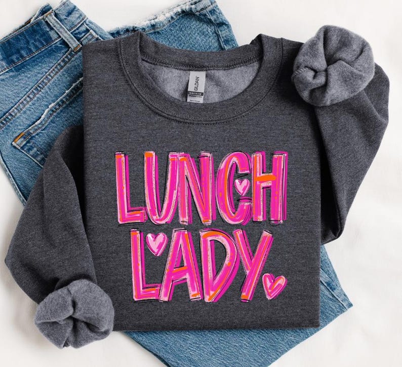 May include: A dark gray sweatshirt with the text "Lunch Lady" in pink and white lettering with pink hearts.