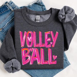 May include: A dark gray sweatshirt with the words "VOLLEYBALL" in pink and orange letters with hearts. The letters are outlined in white.