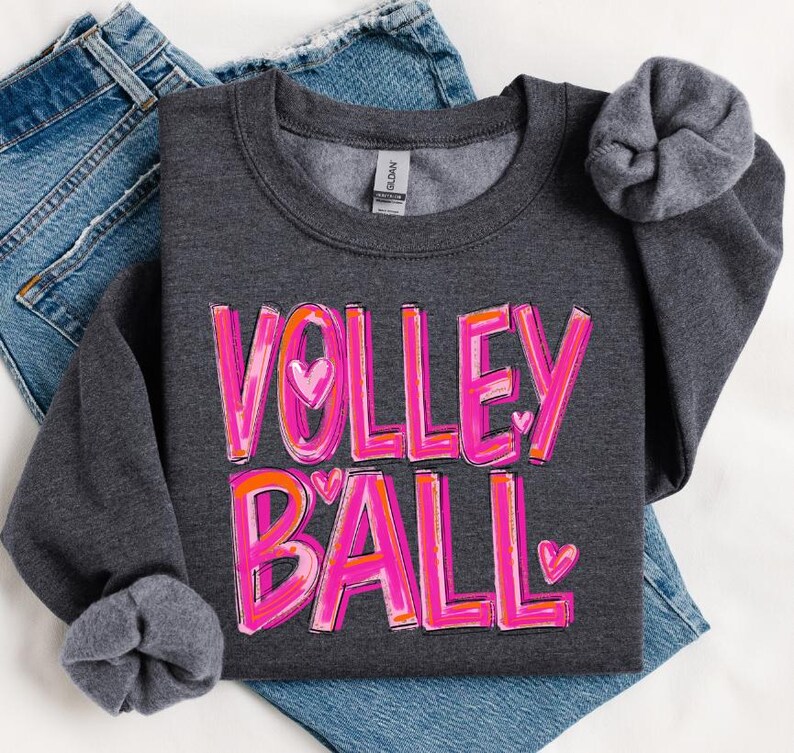 May include: A dark gray sweatshirt with the words "VOLLEYBALL" in pink and orange letters with hearts. The letters are outlined in white.
