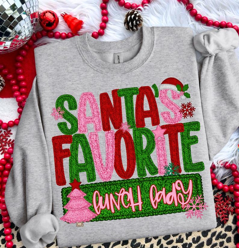 May include: A heather gray sweatshirt with the text "SANTA'S FAVORITE LUNCH LADY" in green, red, and pink. The design includes a Santa hat, snowflakes, and a pink Christmas tree. Festive apparel for the holiday season.