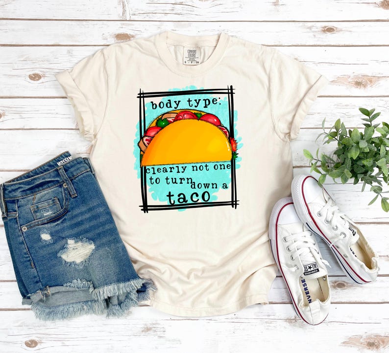 May include: A beige t-shirt with a graphic of a taco and the text "body type: clearly not one to turn down a taco".