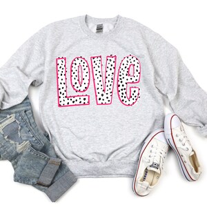 May include: A gray sweatshirt with the word "LOVE" printed in black and white polka dots with a pink outline.