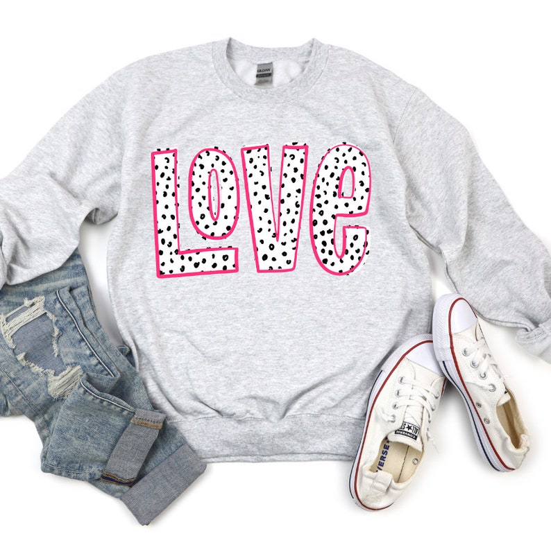 May include: A gray sweatshirt with the word "LOVE" printed in black and white polka dots with a pink outline.