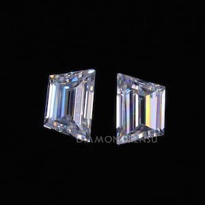 May include: Two clear, faceted, emerald cut gemstones on a black background. The gemstones are rectangular with pointed corners.