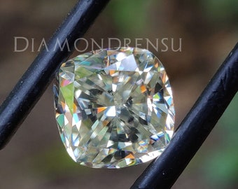 Könnte beinhalten: Ein Diamant-Edelstein im Kissen-Schliff, der mit einer Pinzette gehalten wird. Der Diamant ist klar mit einem leichten Gelbstich und hat einen brillanten Glanz.