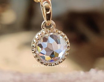 May include: A gold-colored pendant necklace with a round, faceted, clear gemstone. The gemstone is surrounded by a beaded gold bezel. The necklace chain is also gold. The pendant hangs from a small gold loop.