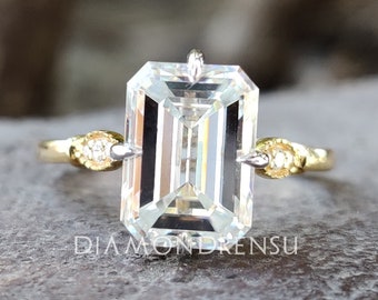 May include: A gold engagement ring with a large, clear emerald-cut diamond and two smaller diamonds on the band.