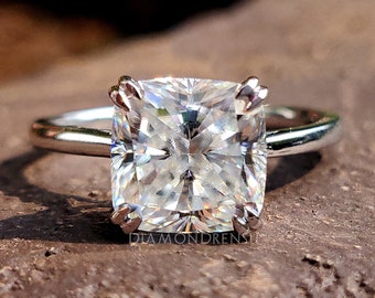 May include: A silver ring with a large, clear, square-shaped diamond. The diamond has a cushion cut and is set in a four-prong setting.
