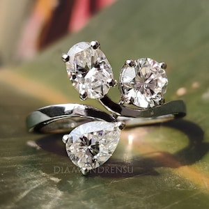 May include: A silver ring with three pear-shaped diamonds. The ring has a unique design with the diamonds set in a curved, vine-like pattern.
