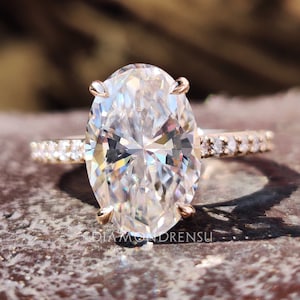 May include: A rose gold engagement ring with a large oval-shaped diamond center stone and a pave diamond band.