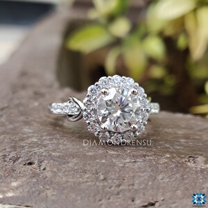 May include: A silver engagement ring featuring a large round centre stone encircled by a halo of smaller stones. The ring has a twisted band with smaller stones set along the sides.