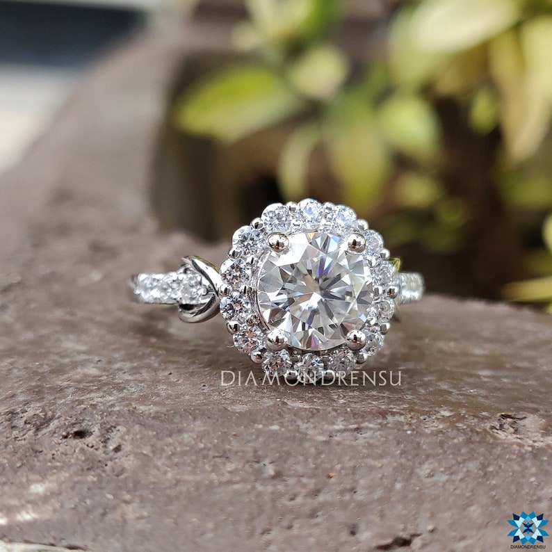 May include: A silver engagement ring featuring a large round centre stone encircled by a halo of smaller stones. The ring has a twisted band with smaller stones set along the sides.