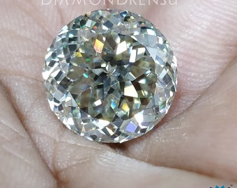 May include: A round, clear, faceted gemstone with a rainbow-like iridescence. The gemstone is held in a hand.