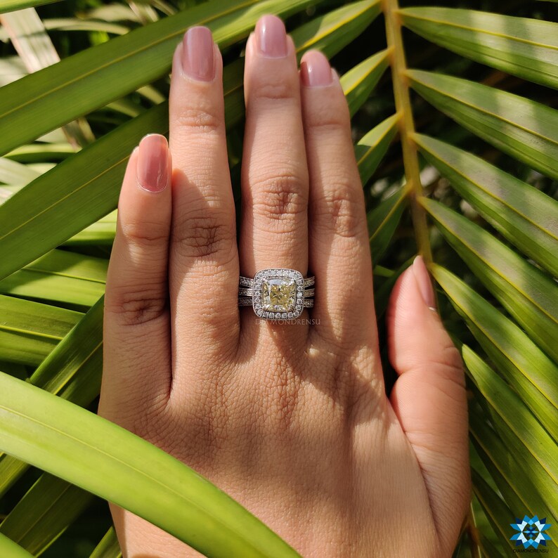 Cushion cut engagement ring shown on a finger under daylight.