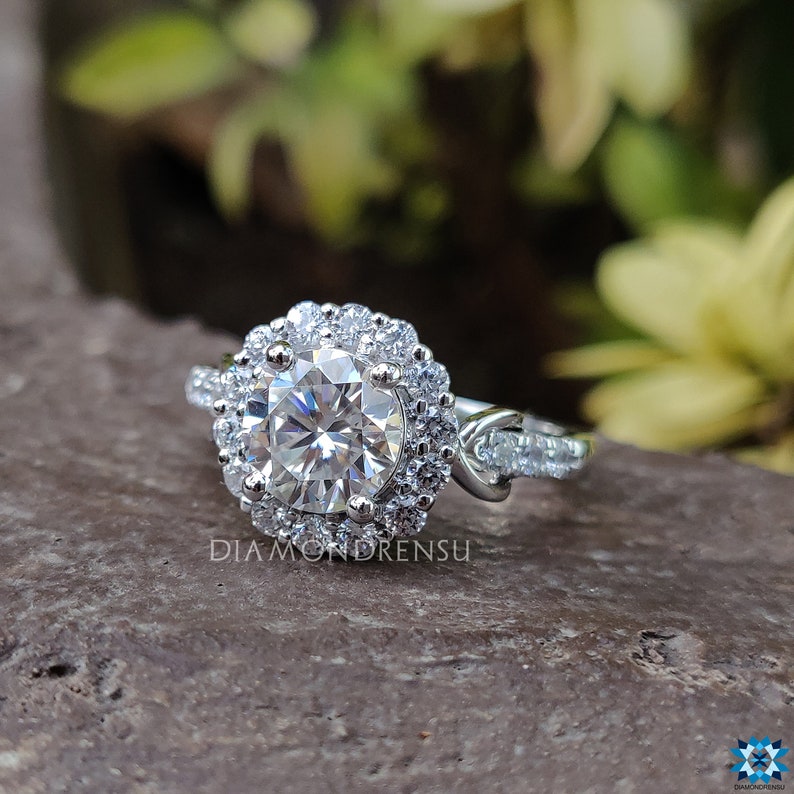 May include: A silver engagement ring featuring a large round centre stone encircled by a double halo of smaller stones. The band is twisted and set with additional smaller stones.