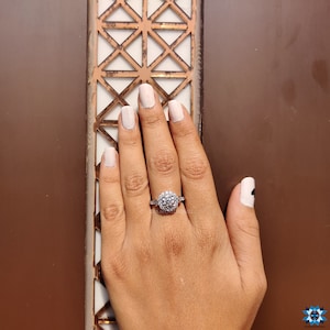 May include: A silver ring featuring a large round cluster of clear stones. The ring is worn on a finger with light pink nail polish.