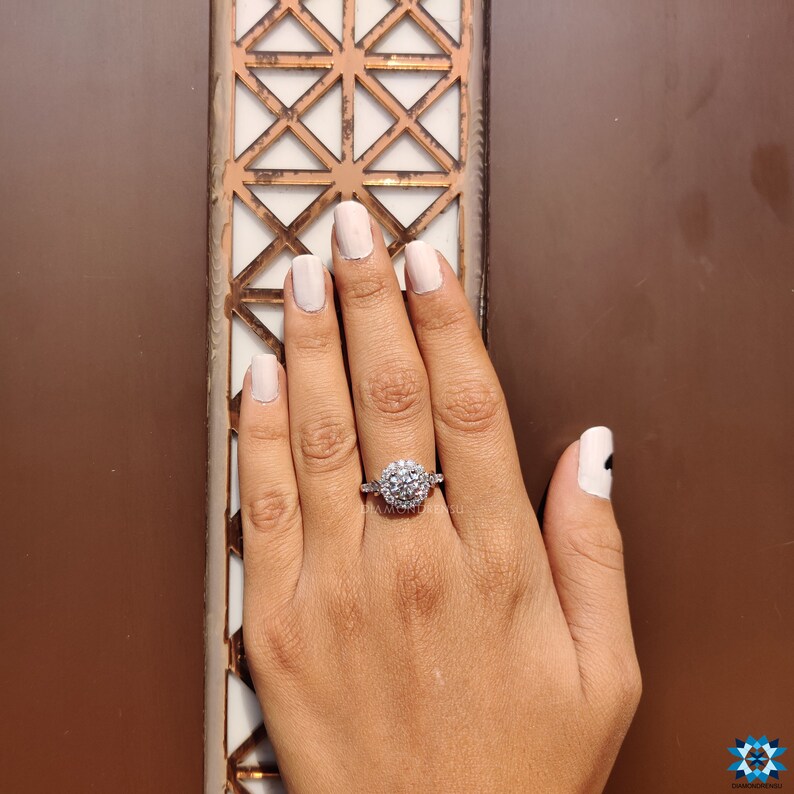 May include: A silver ring featuring a large round cluster of clear stones. The ring is worn on a finger with light pink nail polish.
