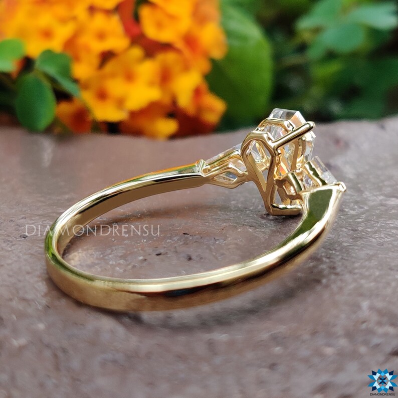 May include: A gold engagement ring with a large, clear, emerald-cut center stone and two smaller, clear, round side stones. The ring is set in a delicate, intricate design.