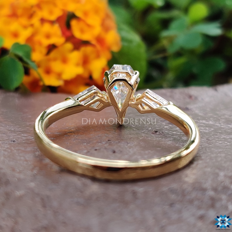 May include: A gold engagement ring with a pear-shaped center stone and baguette side stones. The ring is set on a plain band.