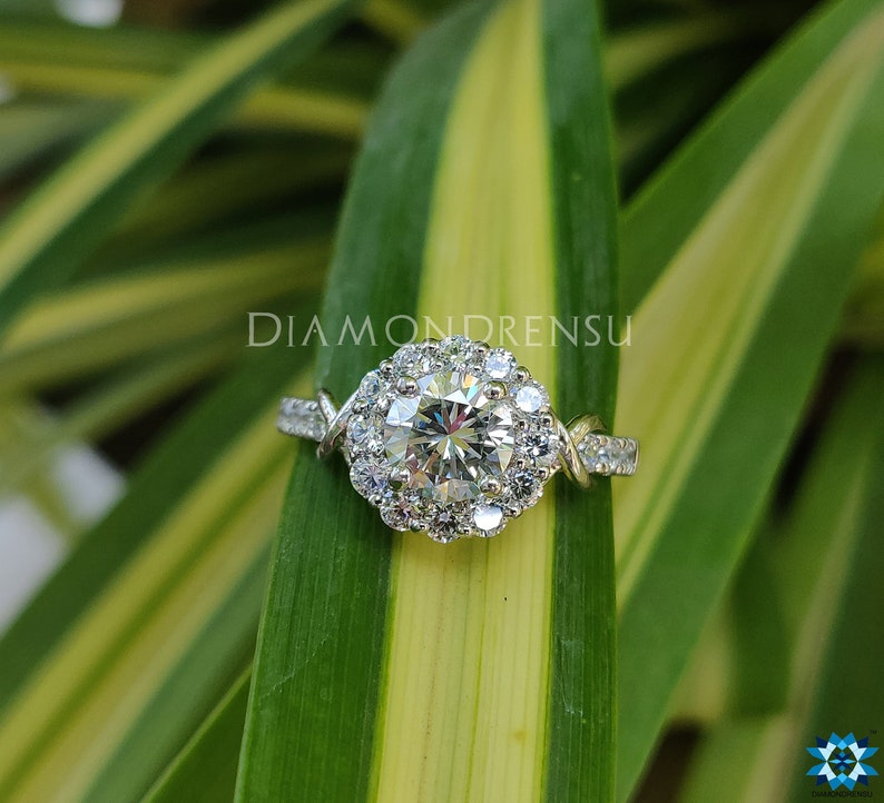 May include: A silver engagement ring featuring a round centre diamond surrounded by a halo of smaller diamonds. The band is twisted and features additional diamonds.