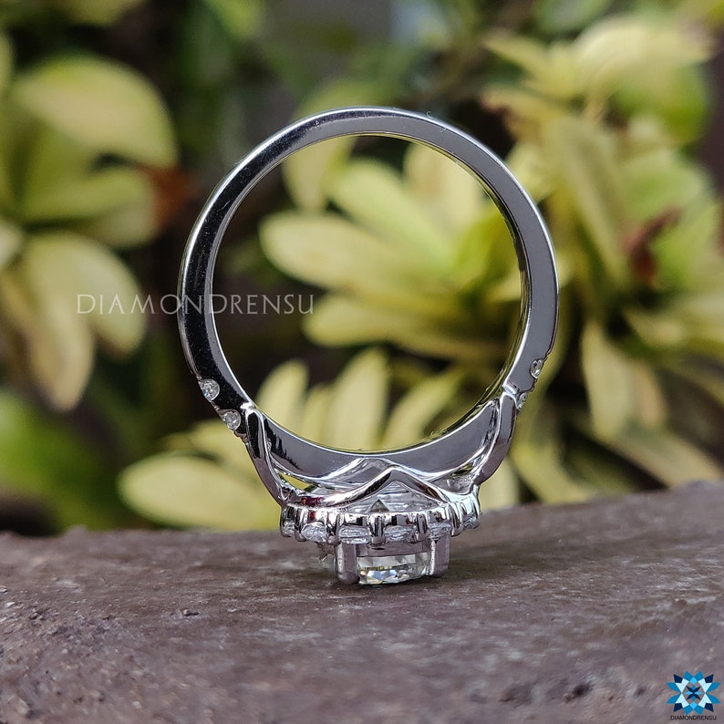 May include: A silver engagement ring featuring a large, round, clear centre stone surrounded by a halo of smaller stones. The ring has a delicate band with small stones set along the sides.