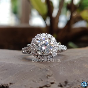 May include: A silver engagement ring featuring a large round centre diamond encircled by a halo of smaller diamonds. The band is embellished with smaller diamonds and has a delicate, twisted design.