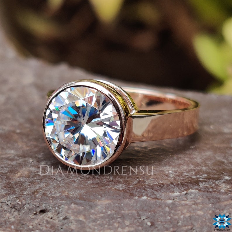Op de afbeelding: Een ring van ros&eacute;goud met een grote, ronde, bezel-gezet, heldere moissanite-steen.