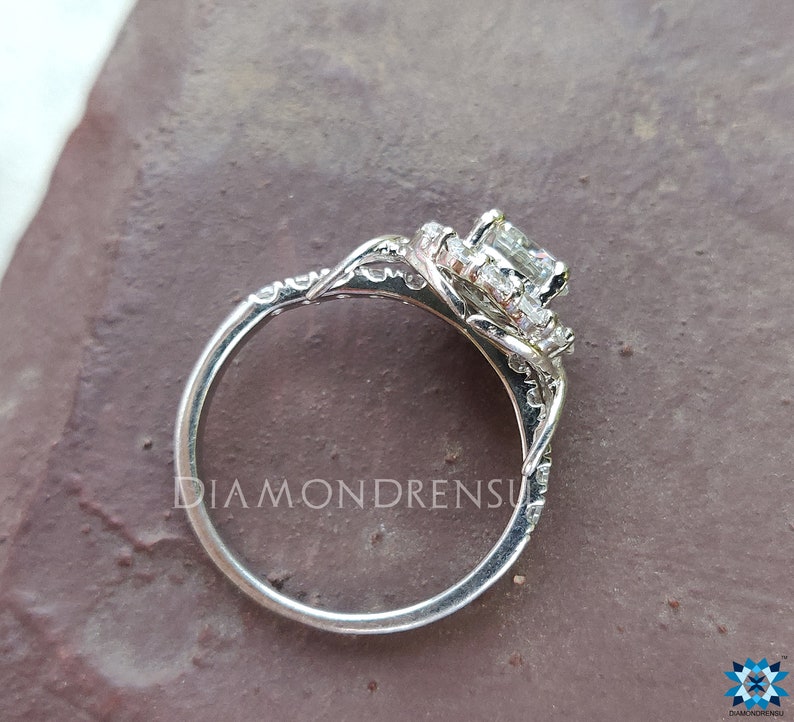 May include: A silver engagement ring featuring a large, square-cut diamond centre stone encircled by a halo of smaller diamonds. The ring has a delicate, intricate design with a twisted band.
