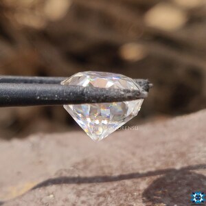 May include: A clear, round, faceted diamond held in tweezers. The diamond has a rainbow-like effect when light shines through it.