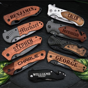 Op de afbeelding: Tien gepersonaliseerde zakmessen met houten handvatten. De handvatten zijn gegraveerd met namen en berichten, zoals "Benjamin, Beste Papa Ooit", "Caleb, Semper Fi", "Michael", "Jeremiah, Blijf Kalm en Anker Vast", "Stephen, Gelukkige Vaderdag", "Charlie", "Christopher", "George" en "Williams, 01.02.2021".