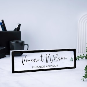 May include: A black acrylic desk nameplate with the text "Vincent Wilson" and "FINANCE ADVISOR" in white lettering.
