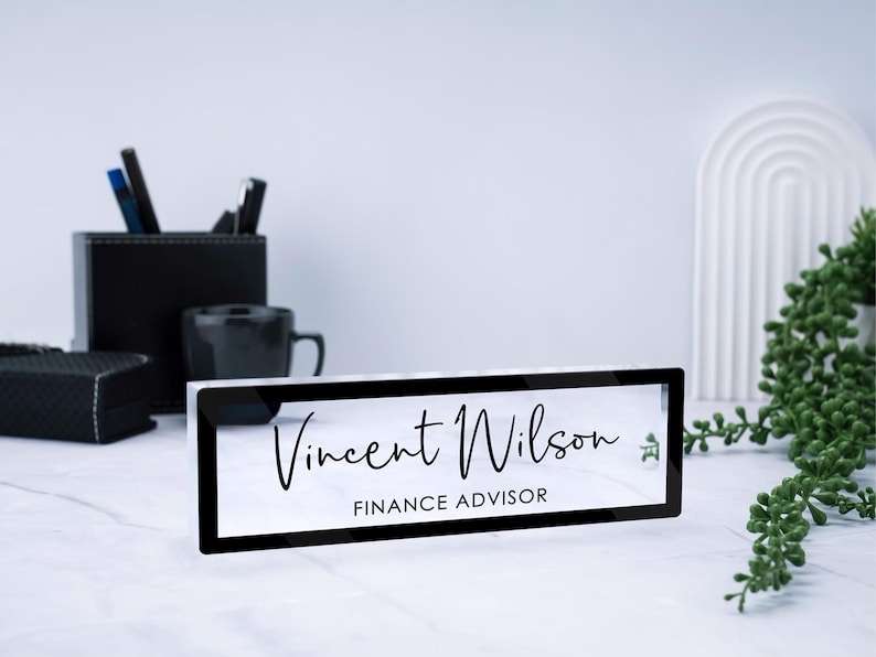 May include: A black acrylic desk nameplate with the text "Vincent Wilson" and "FINANCE ADVISOR" in white lettering.