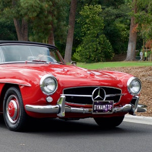 May include: A red classic car with a chrome bumper and a license plate that reads "Dynamite".