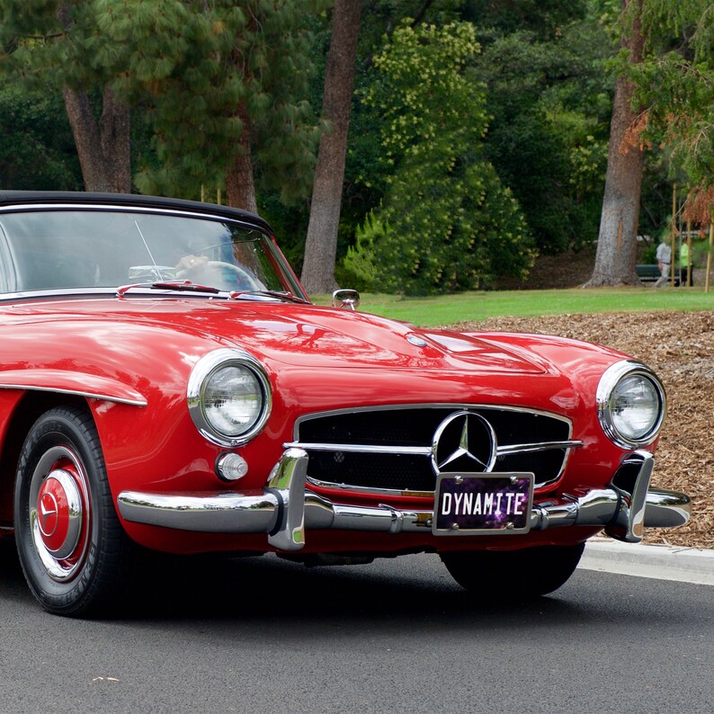 May include: A red classic car with a chrome bumper and a license plate that reads "Dynamite".