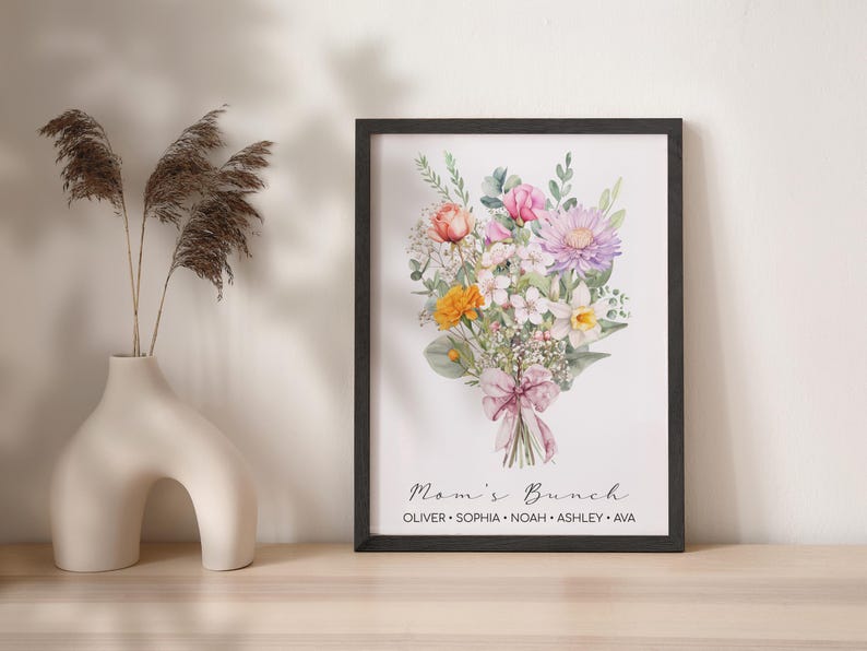 May include: A framed watercolor print of a bouquet of flowers in shades of pink, yellow, and white. The flowers are tied with a pink ribbon and the text "Mom's Brunch" is printed below the bouquet. The names "Oliver, Sophia, Noah, Ashley, Ava" are printed below the text.
