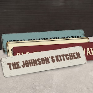 May include: A stack of rectangular, distressed-look signs. The top sign is light blue with the words "THE SECRET ZONE". The middle sign is red with "OLD TOWN" and "VAL". The bottom sign is white with "THE JOHNSON'S KITCHEN".