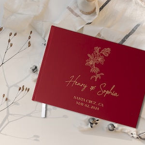 Op de afbeelding: Een bordeauxrood gastenboek met een gouden bloemmotief en de tekst "Henry & Sophia" en "Santa Cruz, CA May 02, 2024".