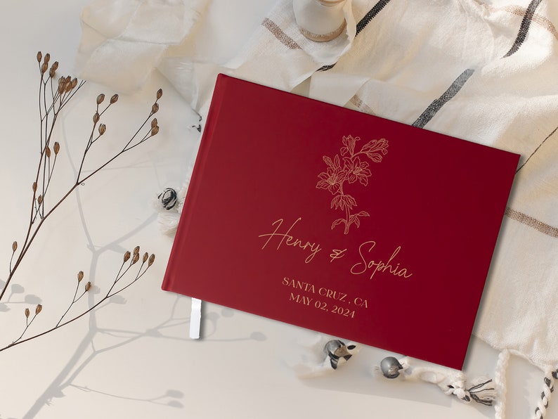 Op de afbeelding: Een bordeauxrood gastenboek met een gouden bloemmotief en de tekst "Henry & Sophia" en "Santa Cruz, CA May 02, 2024".