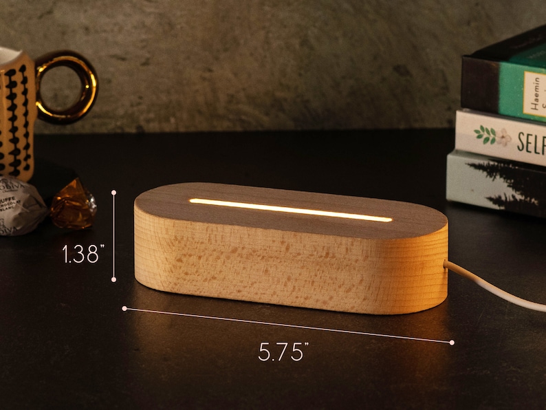 May include: A wooden, oval-shaped LED lamp with a warm, glowing light. The lamp is 5.75 inches long and 1.38 inches high. The light is emitting from a thin slit on the top of the lamp. A white cord extends from the back.