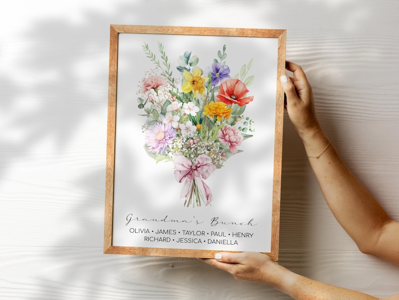 May include: A watercolor print of a bouquet of flowers in a wooden frame. The flowers are in shades of pink, yellow, red, and purple. The text "Grandma's Bunch" is printed below the flowers, followed by a list of names: Olivia, James, Taylor, Paul, Henry, Richard, Jessica, and Daniella.