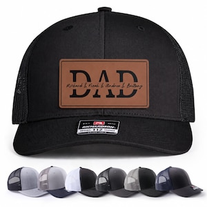 May include: Black trucker hat with a brown leather patch that reads "DAD" with names below. The hat has a mesh back and a curved brim. The Richardson 112 trucker hat is shown in multiple colors.