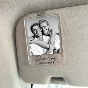 May include: A clear acrylic car visor clip featuring a black and white photo of a smiling couple. The text "Drive Safe" and "LOVE, GIANNA" are printed on the clip, along with a small heart symbol.