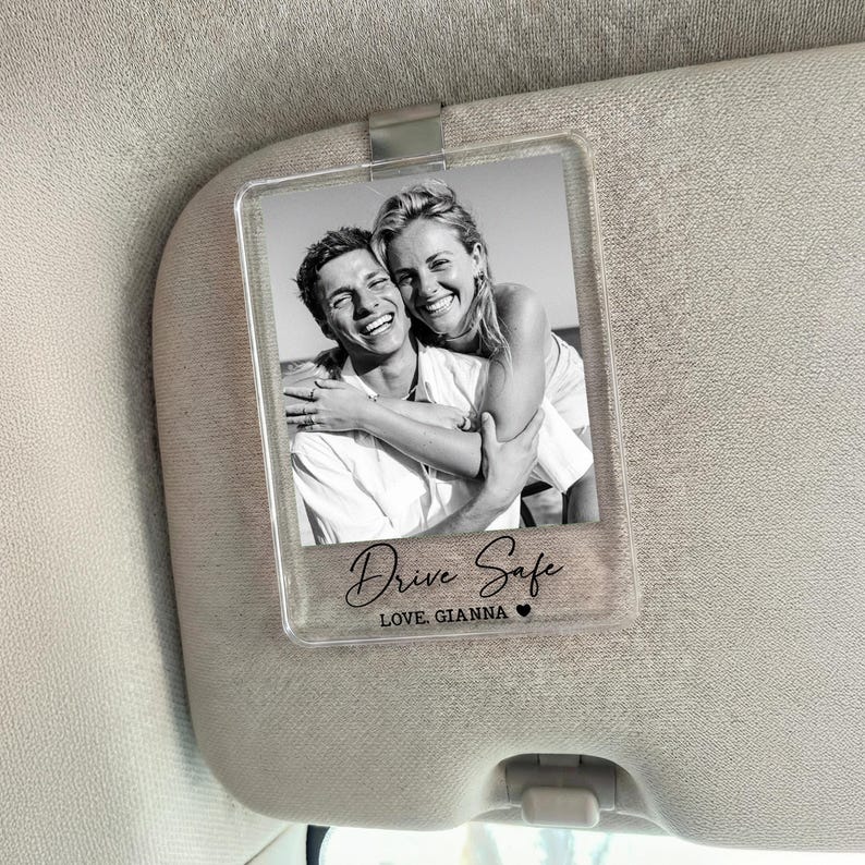 May include: A clear acrylic car visor clip featuring a black and white photo of a smiling couple. The text "Drive Safe" and "LOVE, GIANNA" are printed on the clip, along with a small heart symbol.