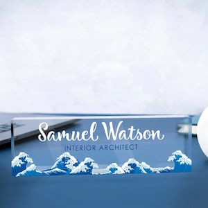 May include: A clear acrylic desk nameplate with a blue wave design and the text "Samuel Watson, Interior Architect".