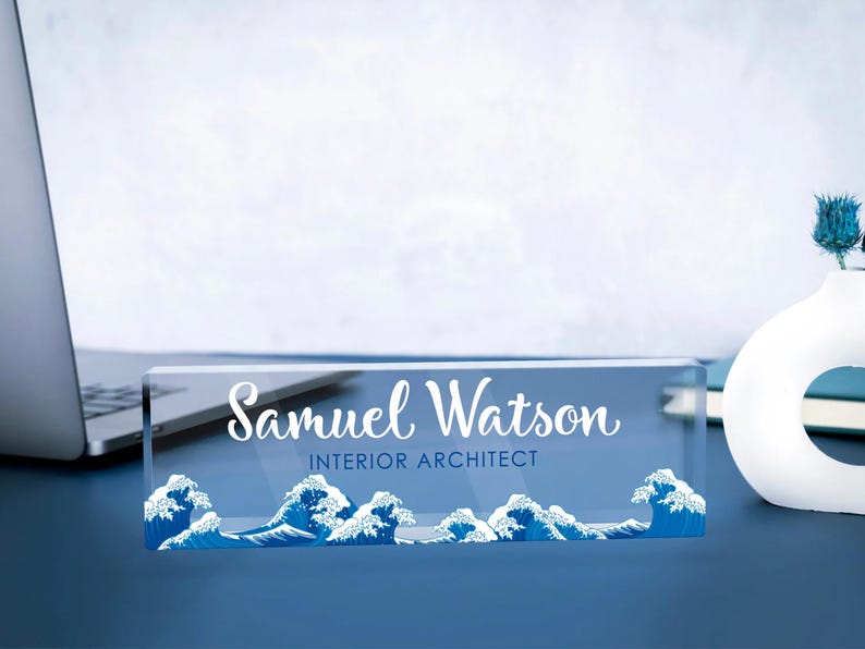 May include: A clear acrylic desk nameplate with a blue wave design and the text "Samuel Watson, Interior Architect".