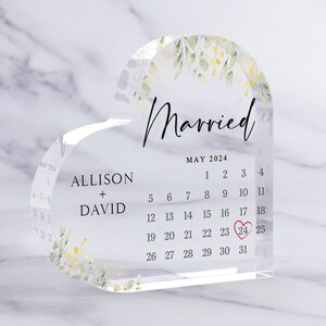 Puede incluir: Un calendario acr&iacute;lico transparente en forma de coraz&oacute;n con un dise&ntilde;o floral y la palabra "Casado" en la parte superior. El calendario es para mayo de 2024 y tiene un coraz&oacute;n rojo marcando el 24.